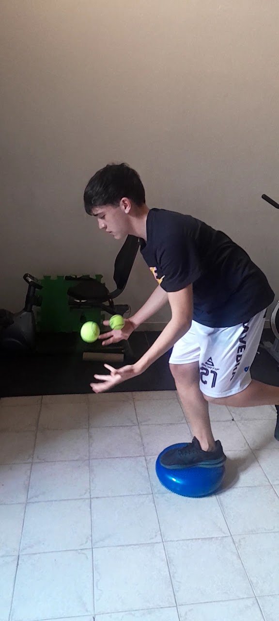 Paciente trabajando equilibrio y coordinación sobre un bosu con pelotas de tenis.